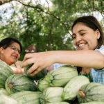 Two Urban Roots youth smile as they sort green squash together.